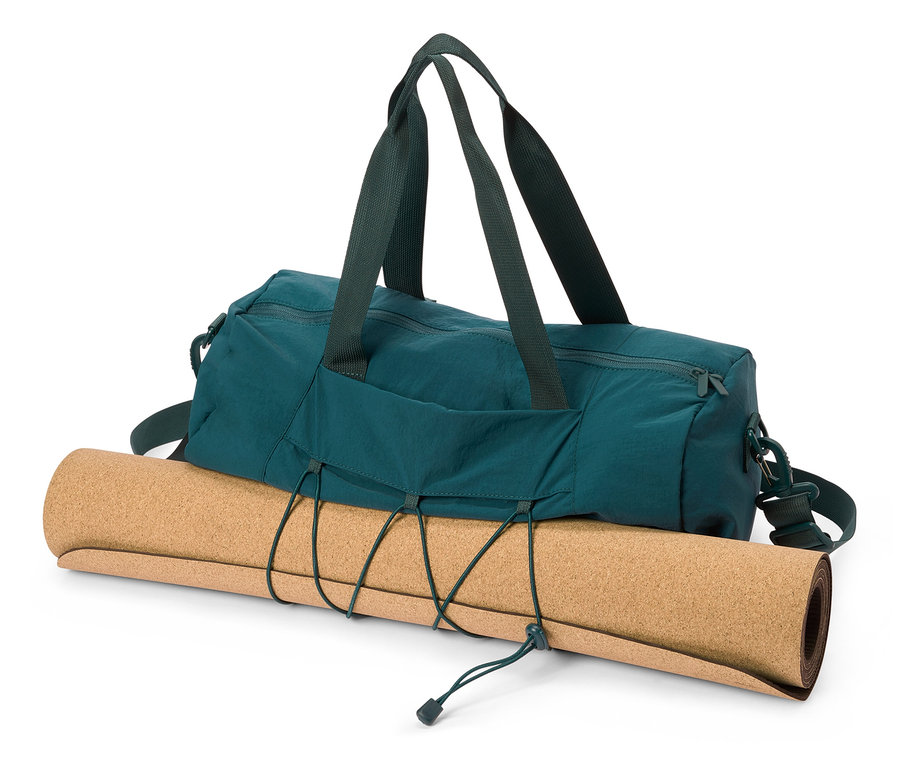 Un sac de sport vert est posé sur un tapis de yoga en liège enroulé.
