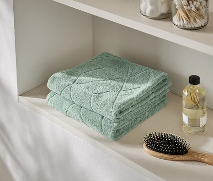 Une pile de serviettes vert menthe repose sur une étagère à côté d'une bouteille d'huile et d'une brosse à cheveux.