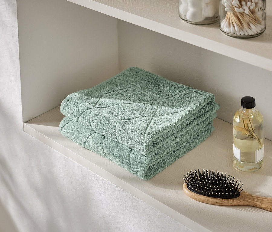 Une pile de serviettes vert menthe repose sur une étagère à côté d'une bouteille d'huile et d'une brosse à cheveux.