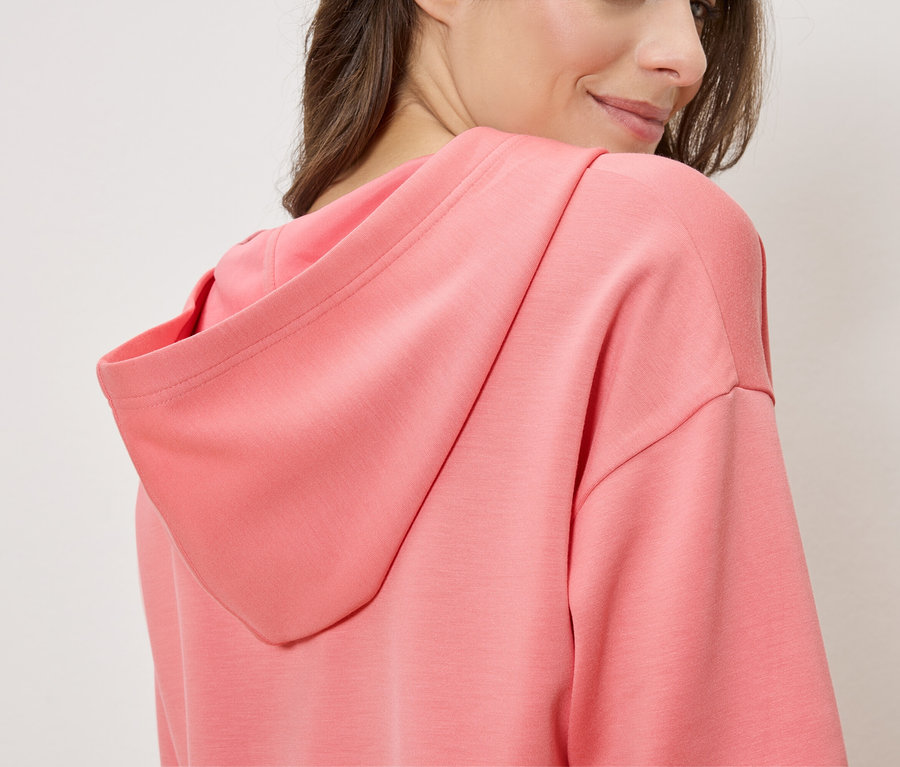 Femme portant un sweat à capuche saumon, vue de côté.