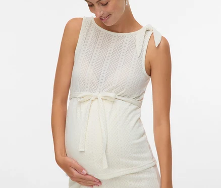 Une femme enceinte dans une robe sans manches avec un ruban et un motif touche son ventre.