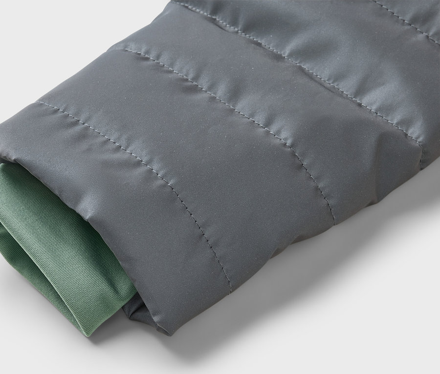 Gros plan sur la manche grise matelassée d'une veste avec un poignet vert sur un fond clair.