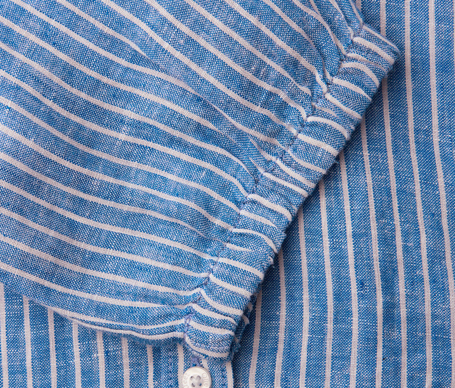 Gros plan d'une chemise rayée bleu et blanc avec bouton et manche.