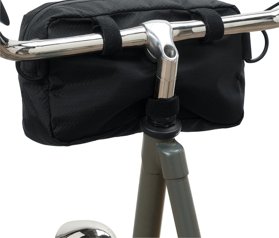 Un sac de guidon de vélo noir fixé à un guidon de vélo argenté par des fermetures auto-agrippantes.