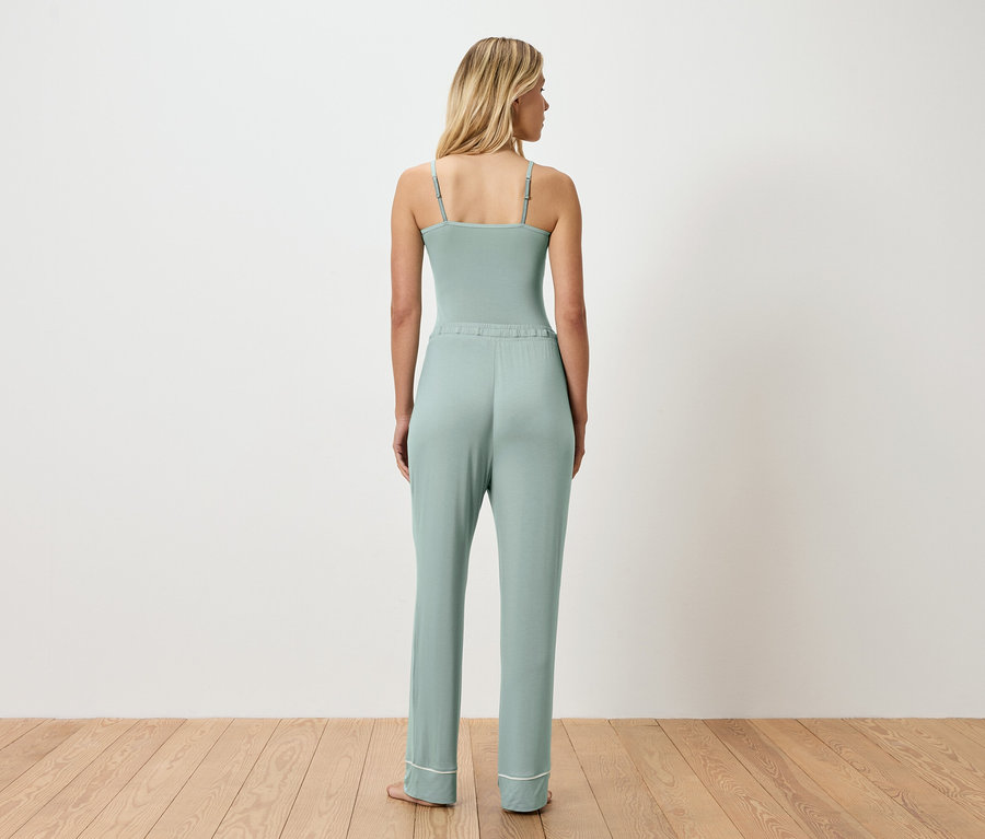 Vue de dos d'une femme blonde portant un body vert clair et un pantalon assorti avec un ourlet blanc.