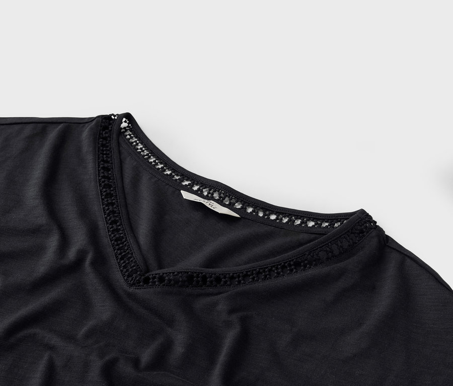 Gros plan d'un t-shirt noir à col en V avec des détails en crochet au niveau de l'encolure.