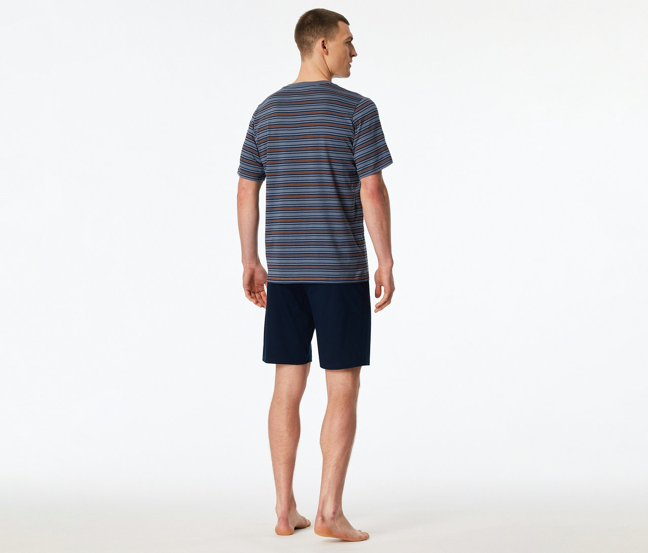 Un homme de dos, portant un set shorty SCHIESSER rayé bleu, marron et gris avec un short bleu marine. Il est pieds nus.