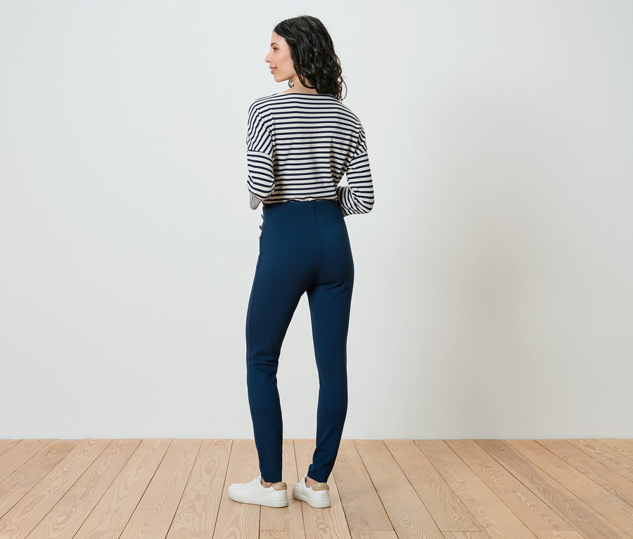 Femme dos à la caméra, portant un haut rayé, un pantalon bleu et des chaussures blanches.