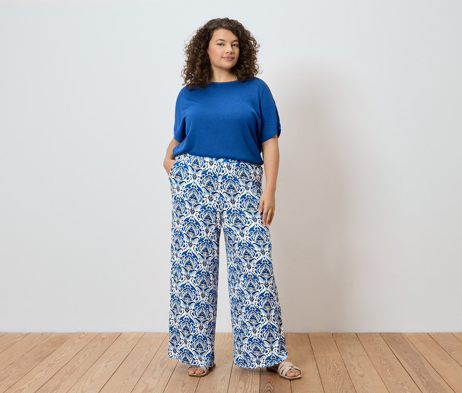 Femme aux cheveux bouclés portant un haut bleu et un pantalon à motifs bleus et blancs.