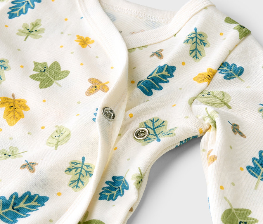 Gros plan d'un pyjama de bébé blanc avec des feuilles colorées et des boutons-pression.