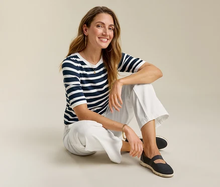 Femme assise par terre en jeans grand confort, un t-shirt rayé et des chaussures foncées.