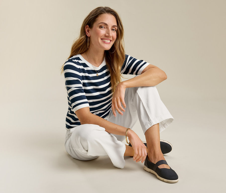 Femme assise par terre en jeans grand confort, un t-shirt rayé et des chaussures foncées.