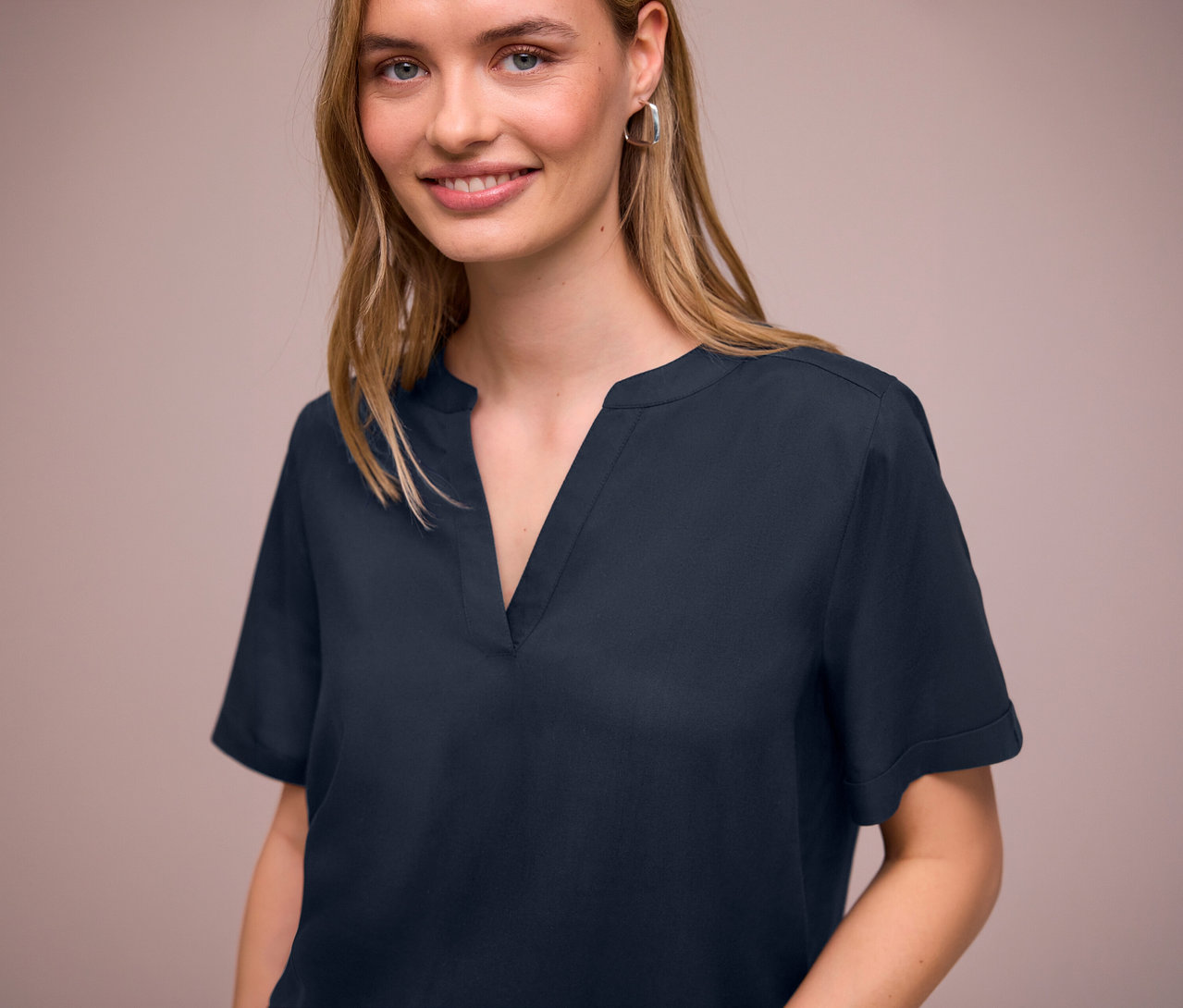 Une femme porte une blouse en maille Street One bleu marine avec un col en V et des boucles d'oreilles argentées.