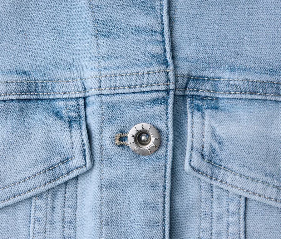 Gros plan d'une veste en jean bleu clair avec des boutons argentés, un col et des poches.