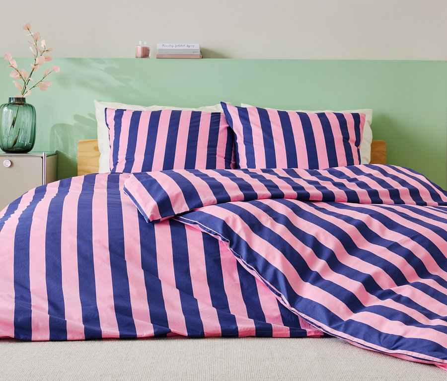 Lit avec des draps rayés bleu et rose, deux oreillers et un mur vert en arrière-plan.