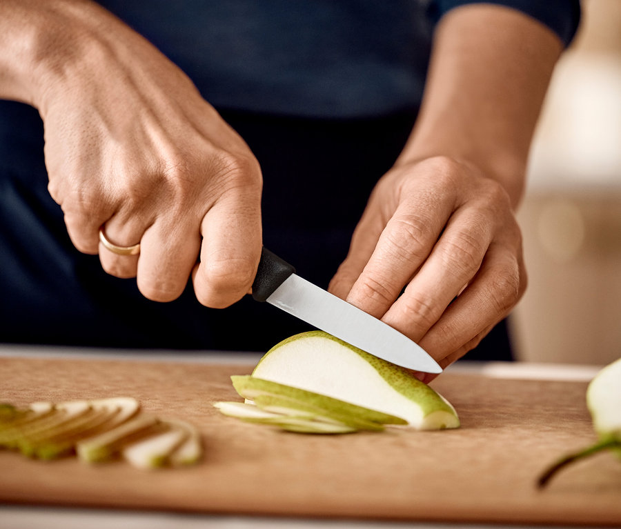 Une personne tranche une poire verte avec un couteau sur une planche à découper.
