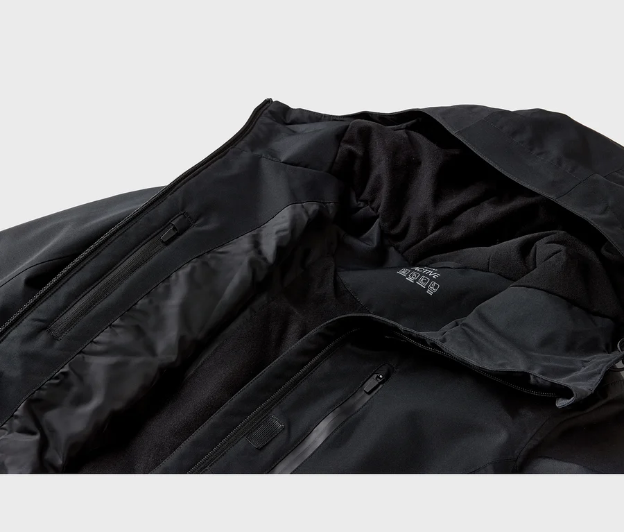 Gros plan d'une veste noire avec une coque extérieure lisse et une doublure intérieure en polaire douce. Des fermetures éclair noires et une étiquette "ACTIVE" sont visibles.