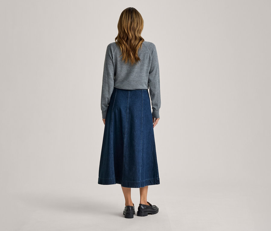 Femme vue de dos, portant un haut gris à manches longues, une jupe midi en jean bleu foncé et des mocassins noirs.