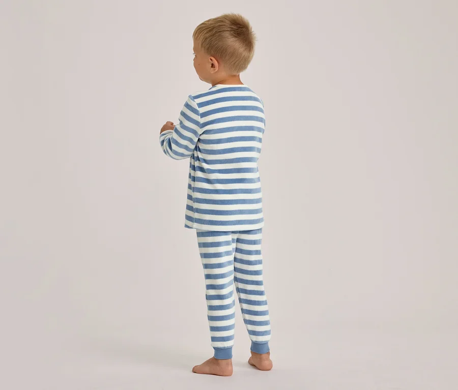 Jeune enfant debout de dos, portant un pyjama rayé bleu et blanc à manches et jambes longues, pieds nus.