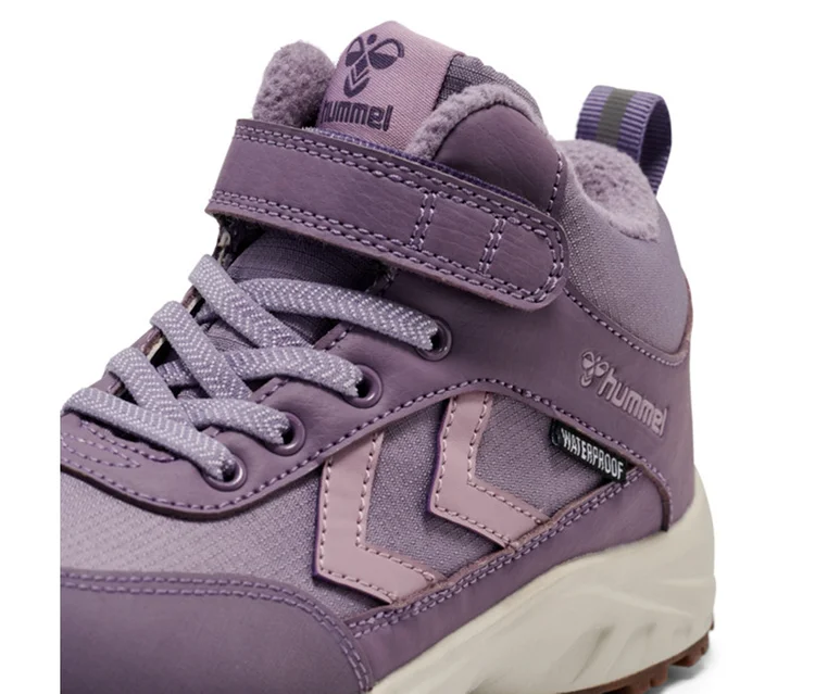 Gros plan d'une basket hummel® « Root Tex Jr » violette avec des chevrons lilas, des lacets et une bande auto-agrippante, avec étiquette "WATERPROOF" et semelle beige.