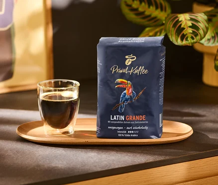 Une tasse de café et un paquet de Privat Kaffee Latin Grande en grains – 500 g sur un plateau en bois.