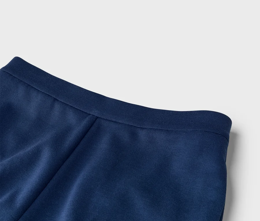 Gros plan d'un tissu bleu marine, montrant une texture lisse et une ceinture ou un ourlet plat en haut. Le tissu présente de légers plis.