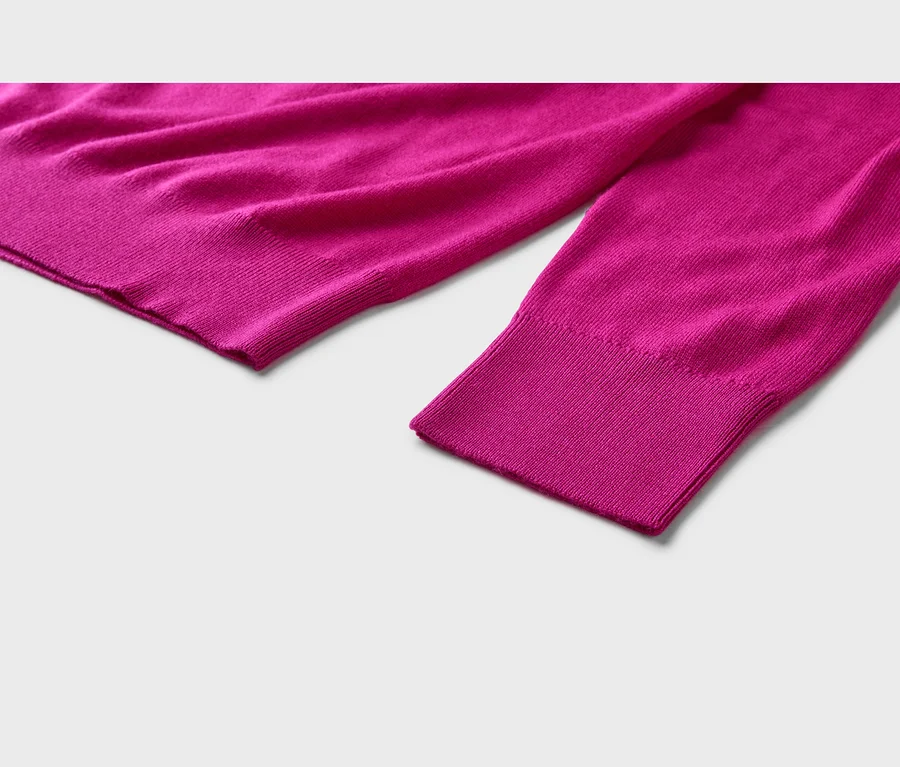 Gros plan d'un pull en maille fuchsia avec des poignets et un ourlet côtelés sur un fond clair.