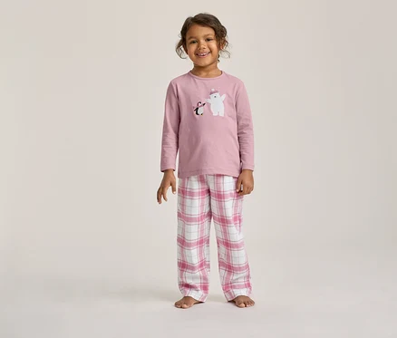 Enfant souriant portant un pyjama rose à manches longues avec un imprimé ours polaire et pingouin, et un pantalon à carreaux roses et blancs.