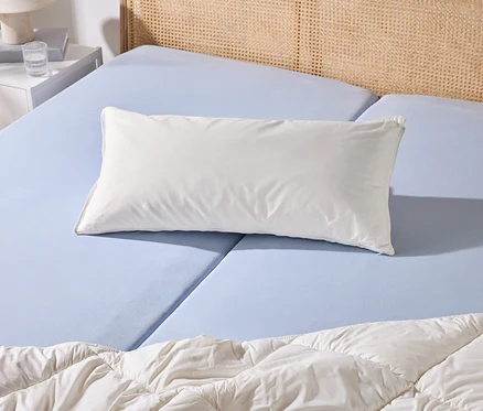 Un lit avec un drap-housse bleu clair, un oreiller blanc et une couette blanche. À côté se trouve une table de chevet blanche avec une lampe et un verre d'eau.