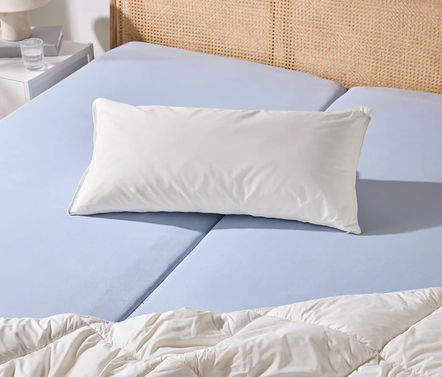 Un lit avec un drap-housse bleu clair, un oreiller blanc et une couette blanche. À côté se trouve une table de chevet blanche avec une lampe et un verre d'eau.
