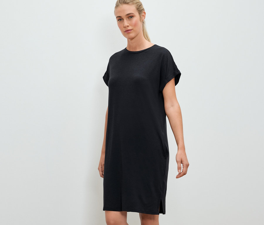 Une femme pose et porte une robe d'extérieur noire.