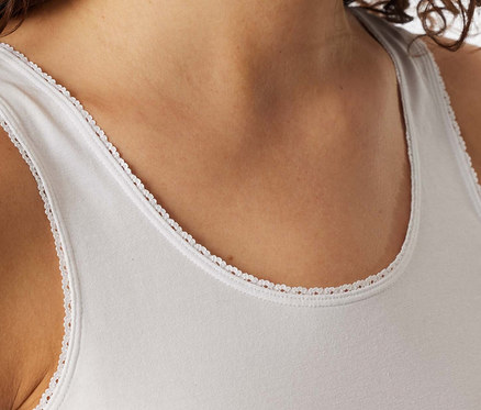 Femme portant un top à bretelles SCHIESSER blanc avec une délicate bordure en dentelle, souriante.