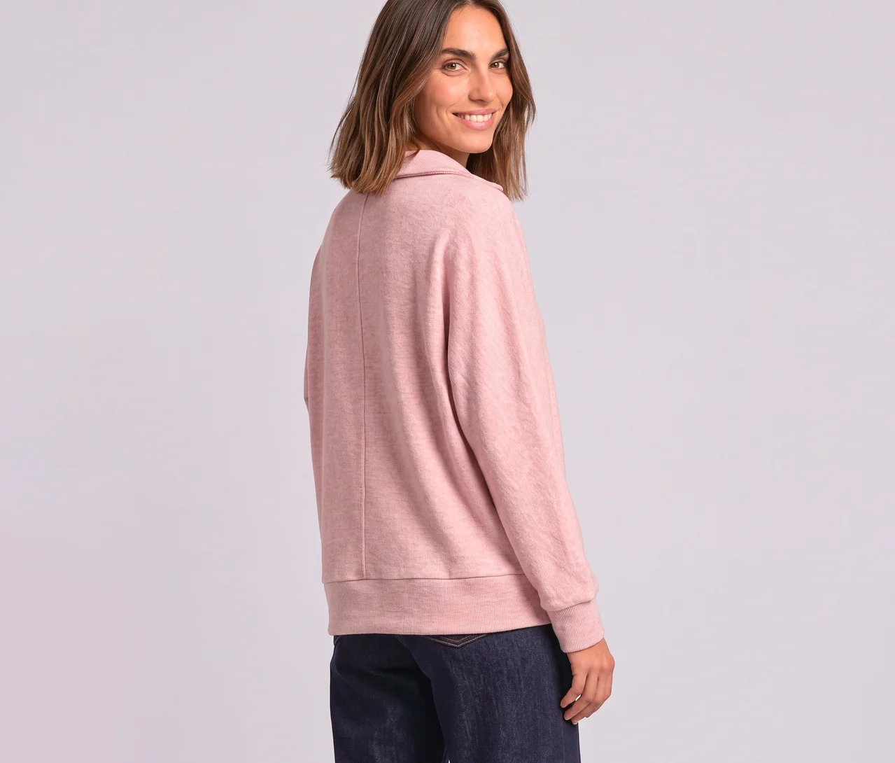 Femme souriante regardant par-dessus son épaule, portant un polo Street One rose à manches longues et un jean foncé.