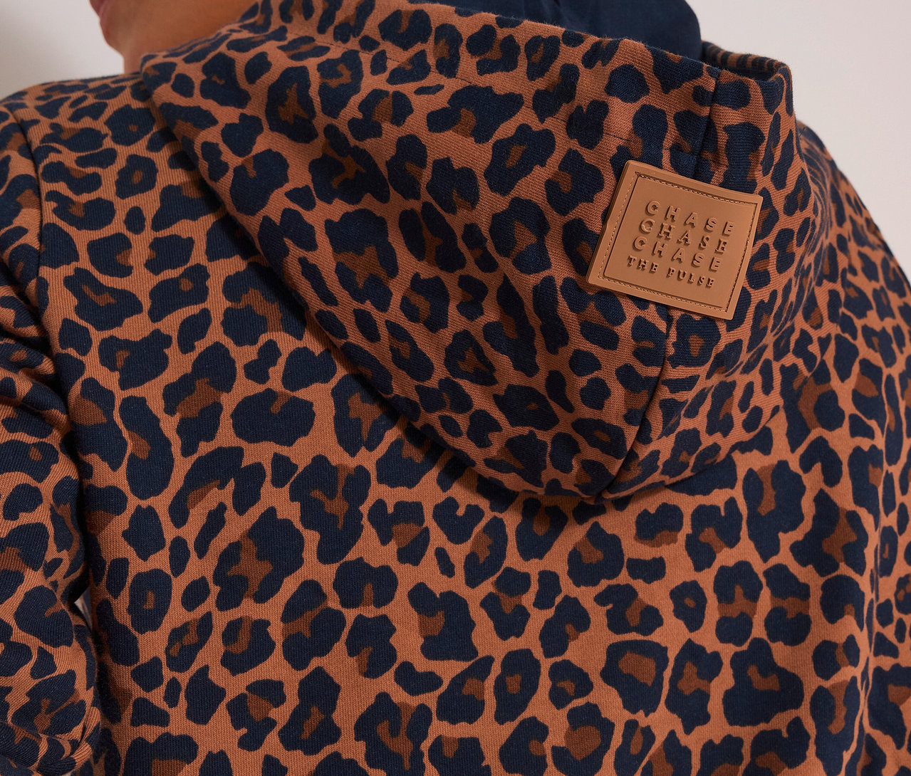 Vue de dos d'une personne portant un sweatshirt CECIL à capuche marron et bleu foncé à imprimé léopard, avec un écusson marron sur la capuche.