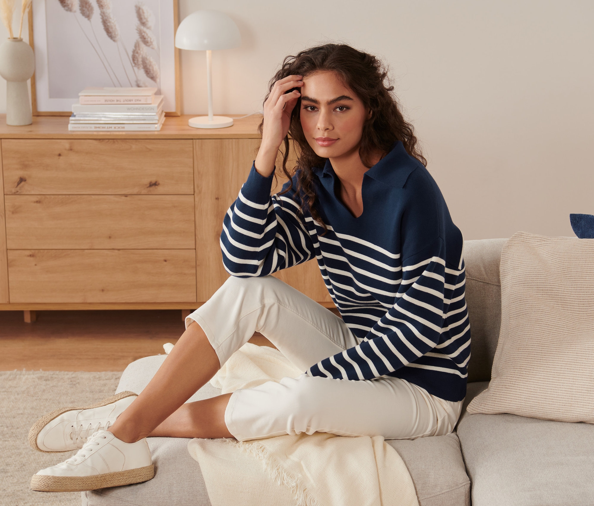 Femme assise sur un canapé portant un pull en maille avec col, bleu et blanc.