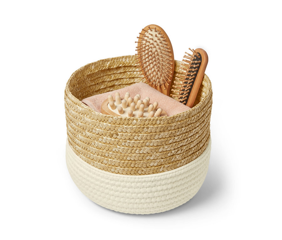 Dans un panier de rangement se trouvent deux brosses à cheveux et une brosse de massage.