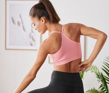 Femme en legging de sport noir et soutien-gorge de sport sans coutures rose debout sur une jambe dans la pose de l'arbre.