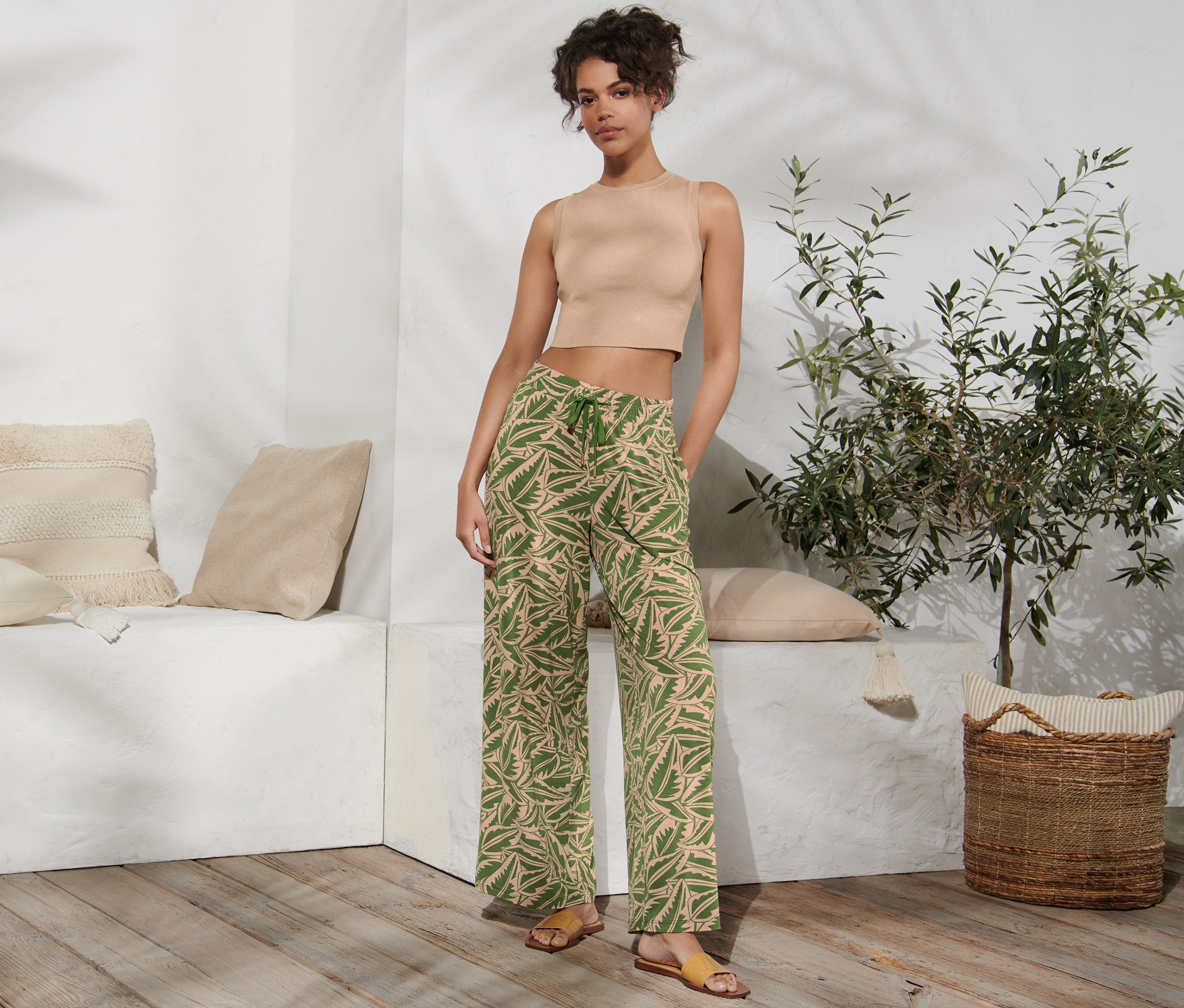 Une femme pose en haut et en pantalon palazzo imprimé vert et beige.