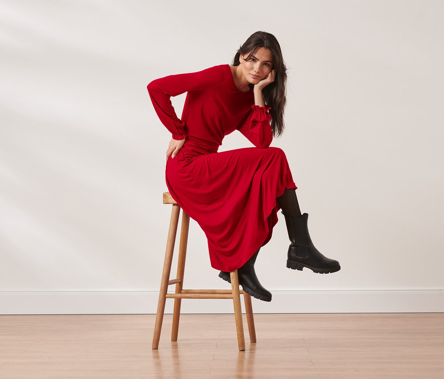 Femme assise sur un tabouret portant une robe en jersey mi-longueur rouge.