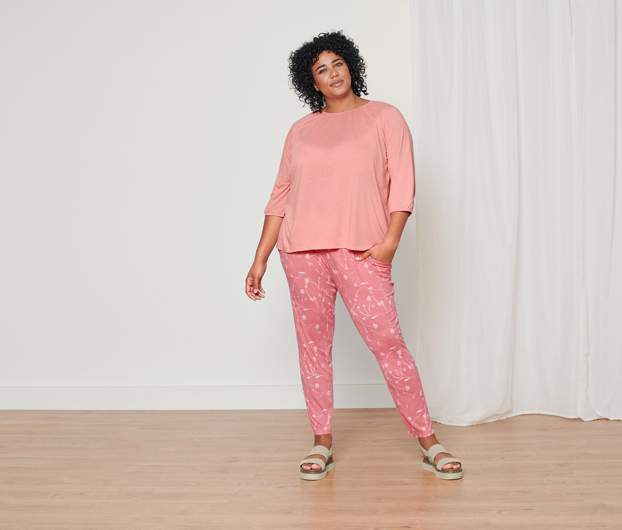 Une femme pose dans un t-shirt corail à manches 3/4, un pantalon en jersey corail avec motif intégral et des sandales à plateau en cuir.