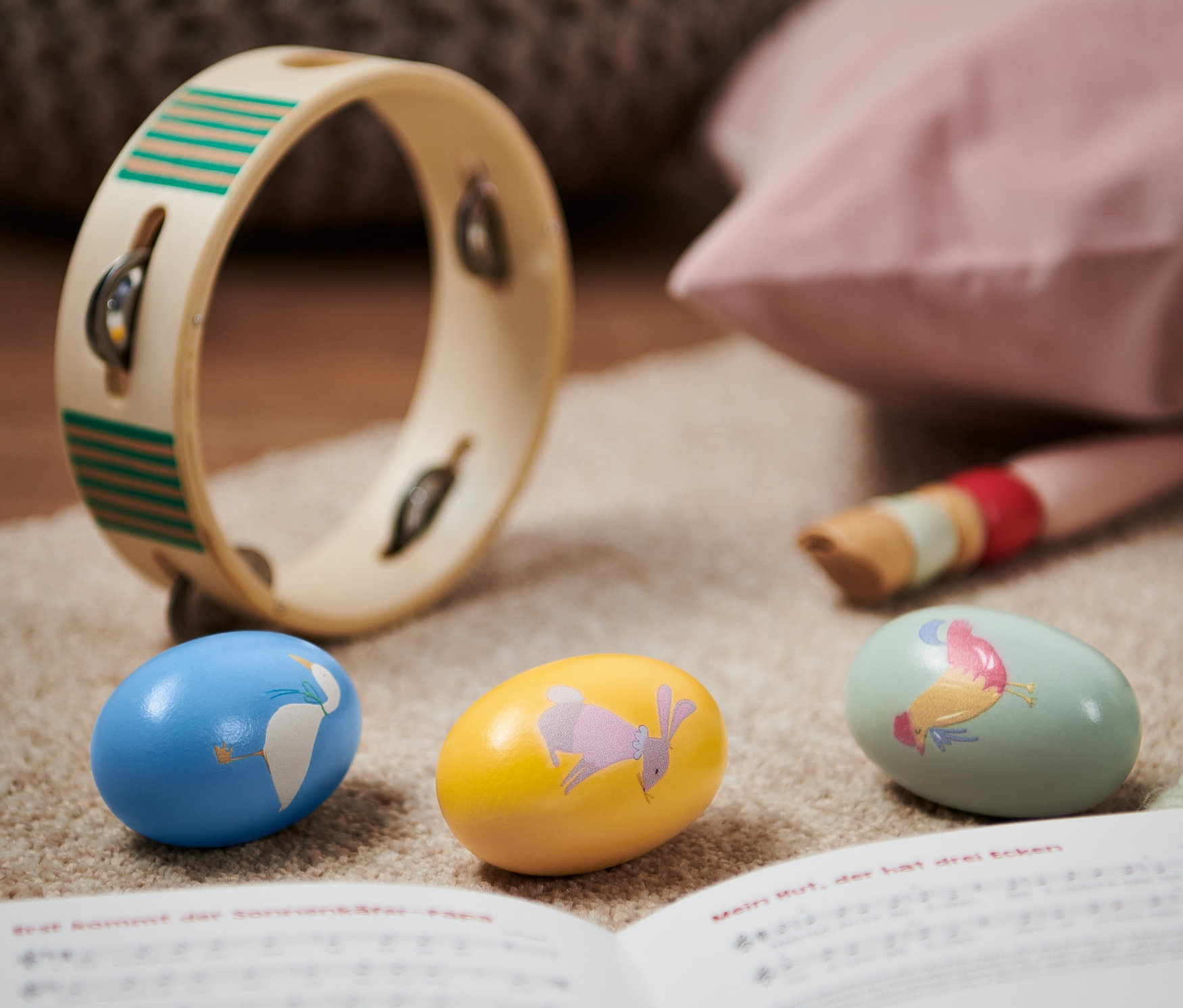 Sur un tapis beige reposent trois maracas, un tambourin et un livre de musique ouvert.