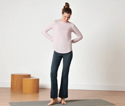 Femme debout sur un tapis de yoga portant un pantalon de sport modelant bleu foncé.