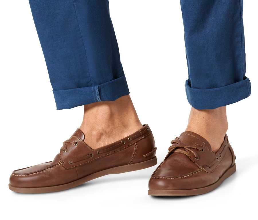 Pieds d'un homme portant un pantalon bleu et des chaussures bateau en cuir.