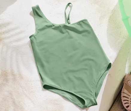 Un maillot de bain pour enfant vert est posé sur du sable blanc à côté d'une bouée gonflable et de sandales.