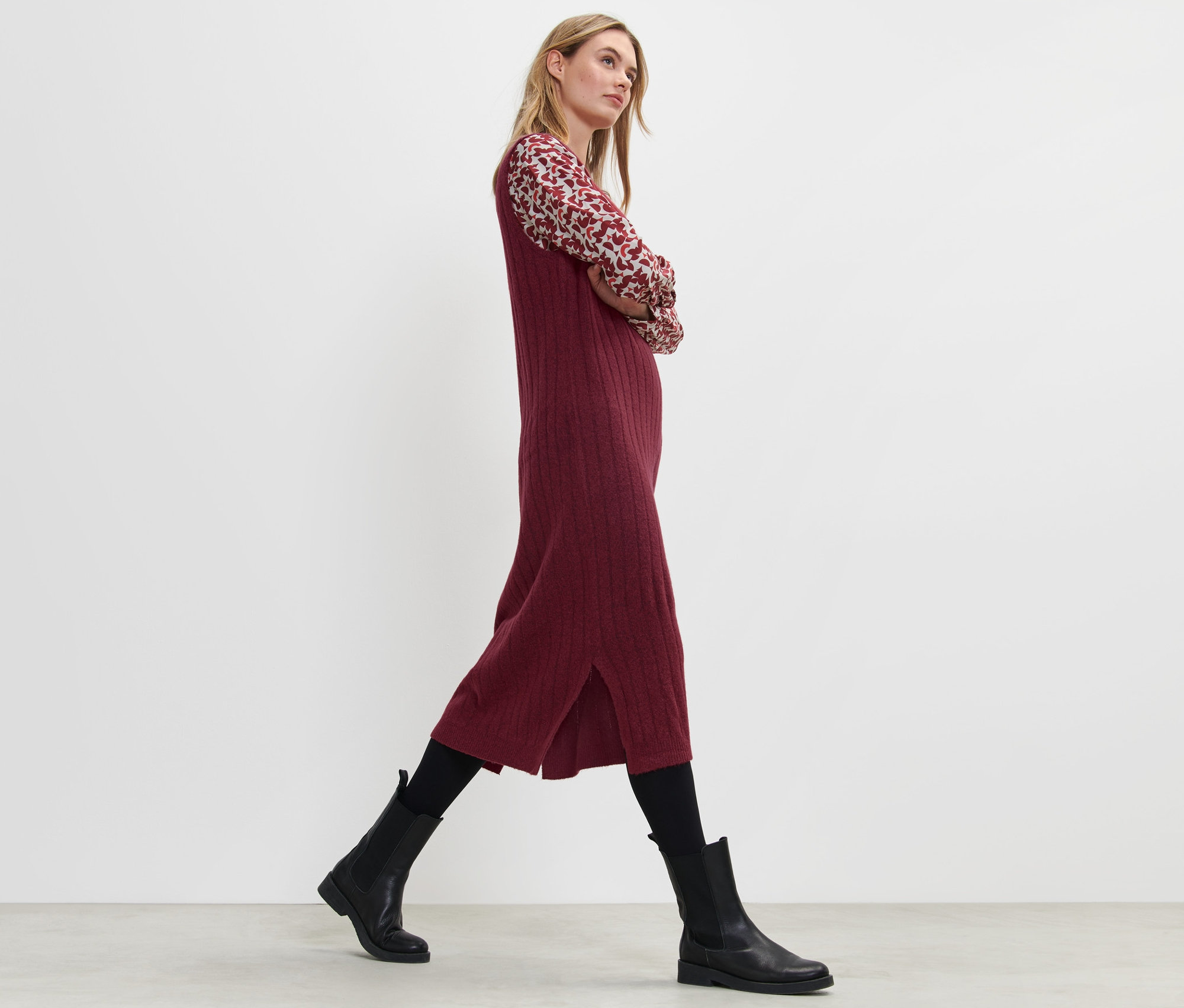 Blonde marchant et portant une robe en tricot côtelée rouge.