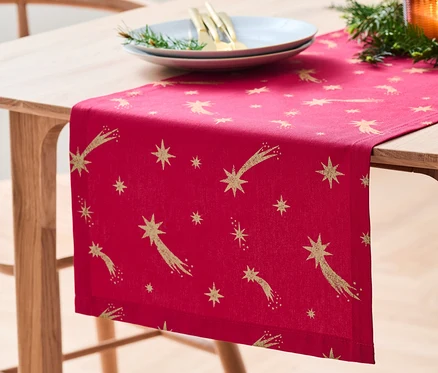Sur une table en bois se trouve un chemin de table en coton avec un imprimé étoiles.