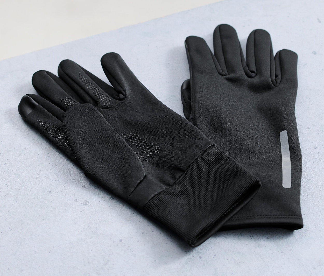 Deux paires de gants thermiques pour protection contre le vent sont posées sur une surface grise, avec une roue de vélo en arrière-plan.