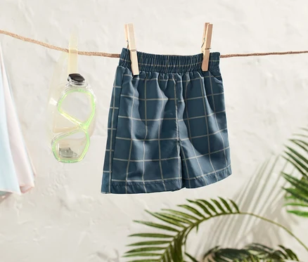 Un boardshort pour tout-petit est suspendu à une corde à linge, à côté de lunettes de plongée et d'un parasol de plage.