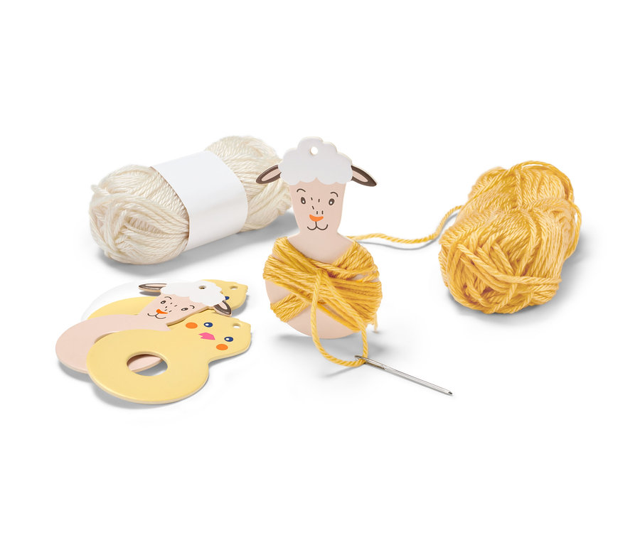 Sur un fond blanc se trouve un kit de construction pour pompons de Pâques avec de la laine jaune et crème, des pochoirs d'animaux et une aiguille.
