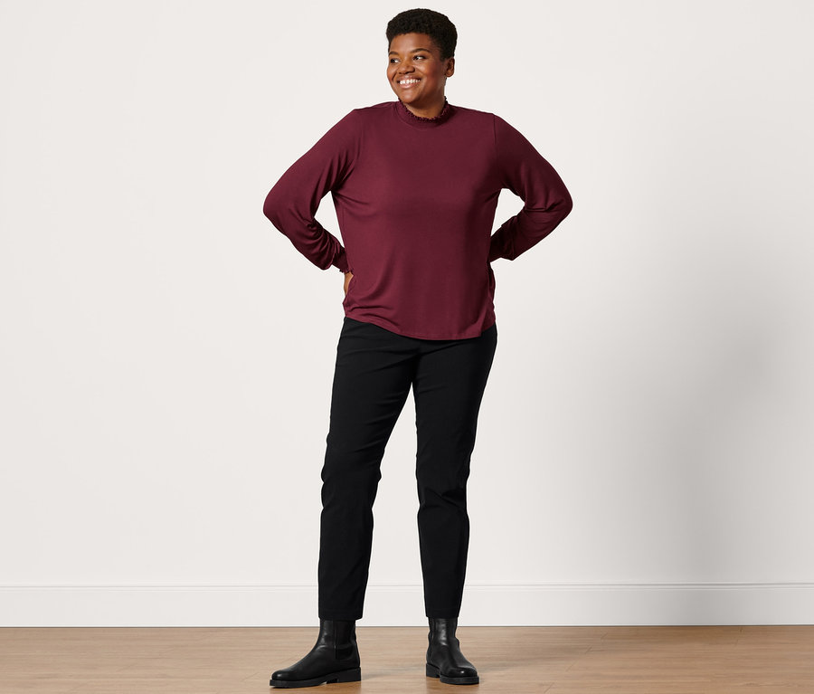 Femme posant en bottines en cuir, pantalon prêt à porter en bengaline noir et blouse à col montant.